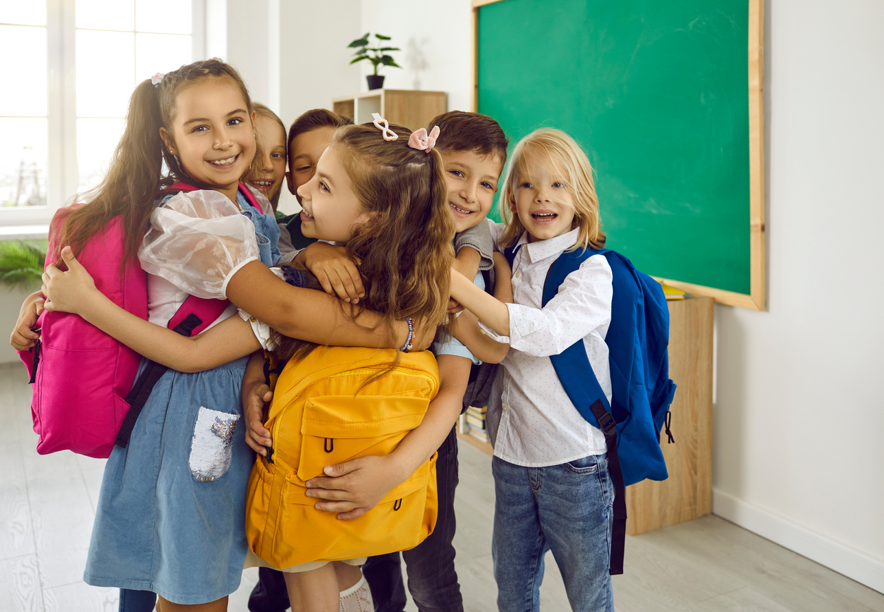 Happy Little Elementary School Students Hugging after Meeting in School Classroom.